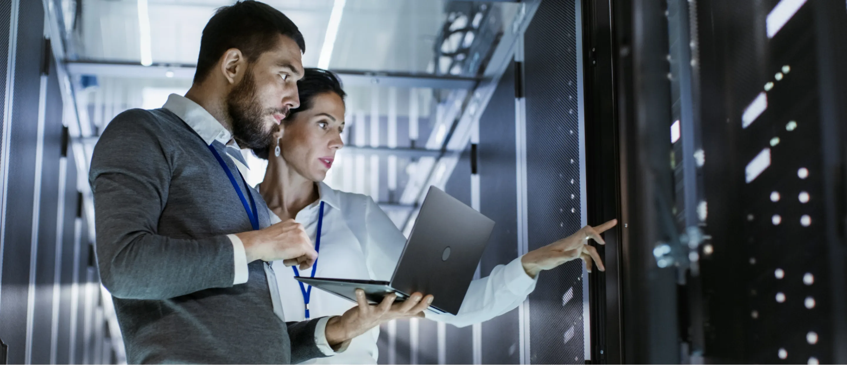 Two colleagues hold a laptop while looking at a data server.