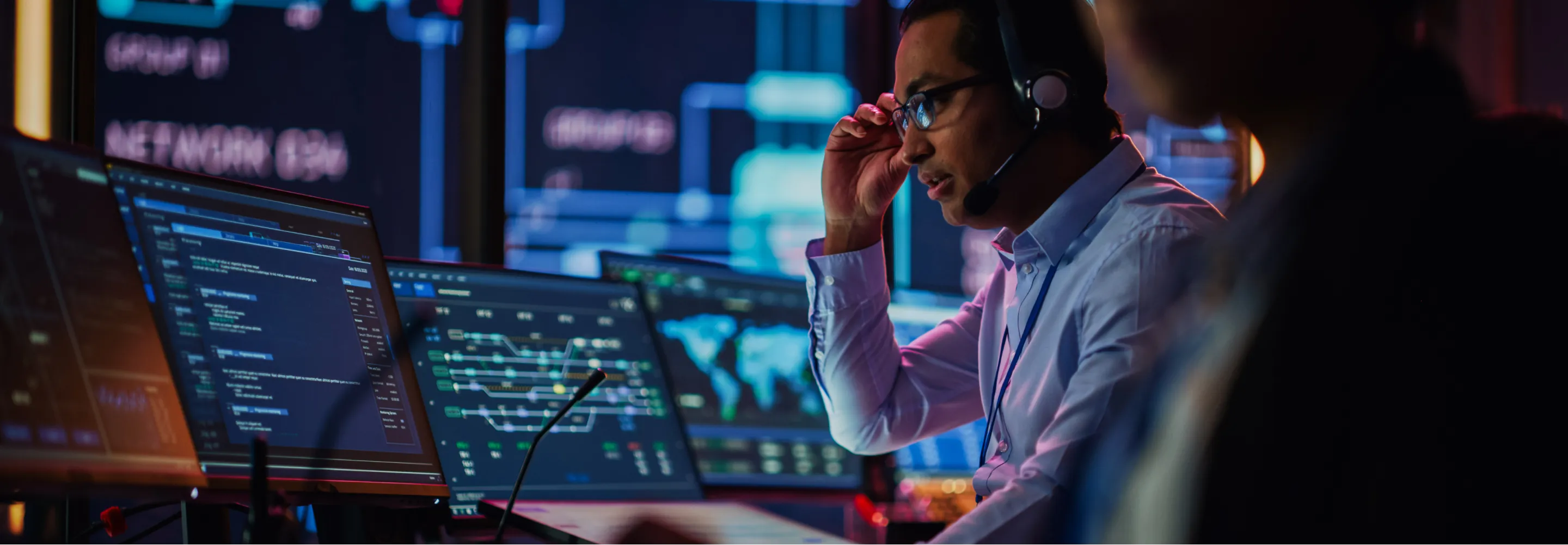 A professional man wearing a headset sitting in front of multiple computer screens.