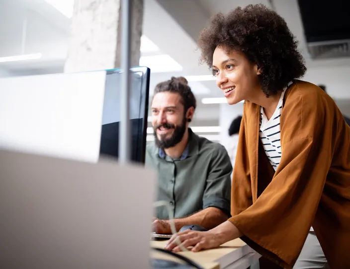 Two colleagues collaborating while typing on a desktop computer in an office.