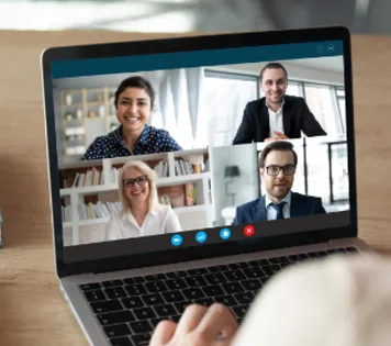 View over a person’s shoulder of a laptop screen with four people on a video conference call with colleagues.
