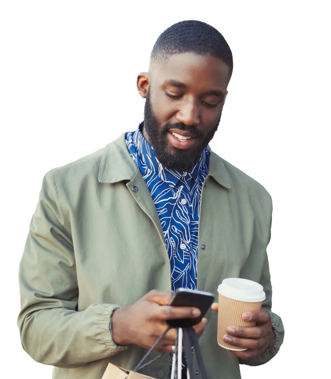 A man wearing a coat and walking outside while looking at his smartphone and holding a disposable coffee cup and shopping bags.