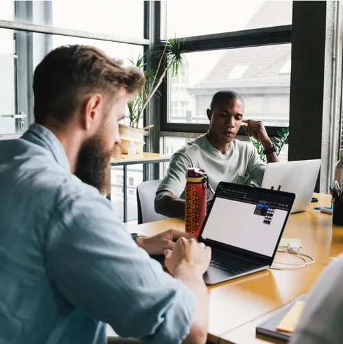 Colleagues sitting at table in a modern office and working on team projects on their laptops.