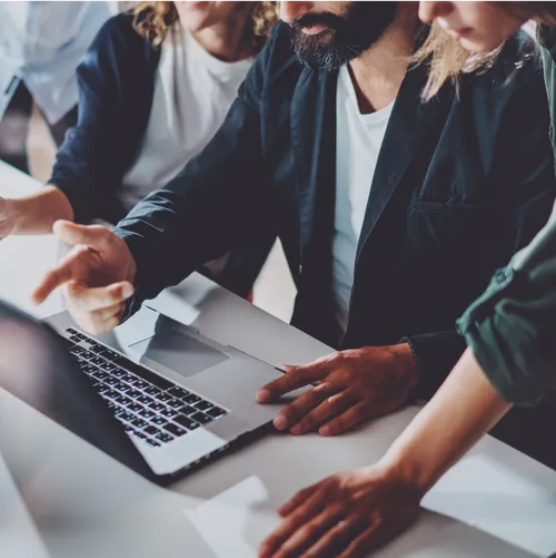 Closeup of three colleagues working together and motioning to a laptop on a desk in front of them. 
