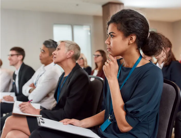 Interested professionals sitting in the audience and taking notes on paper while listening to a presentation.