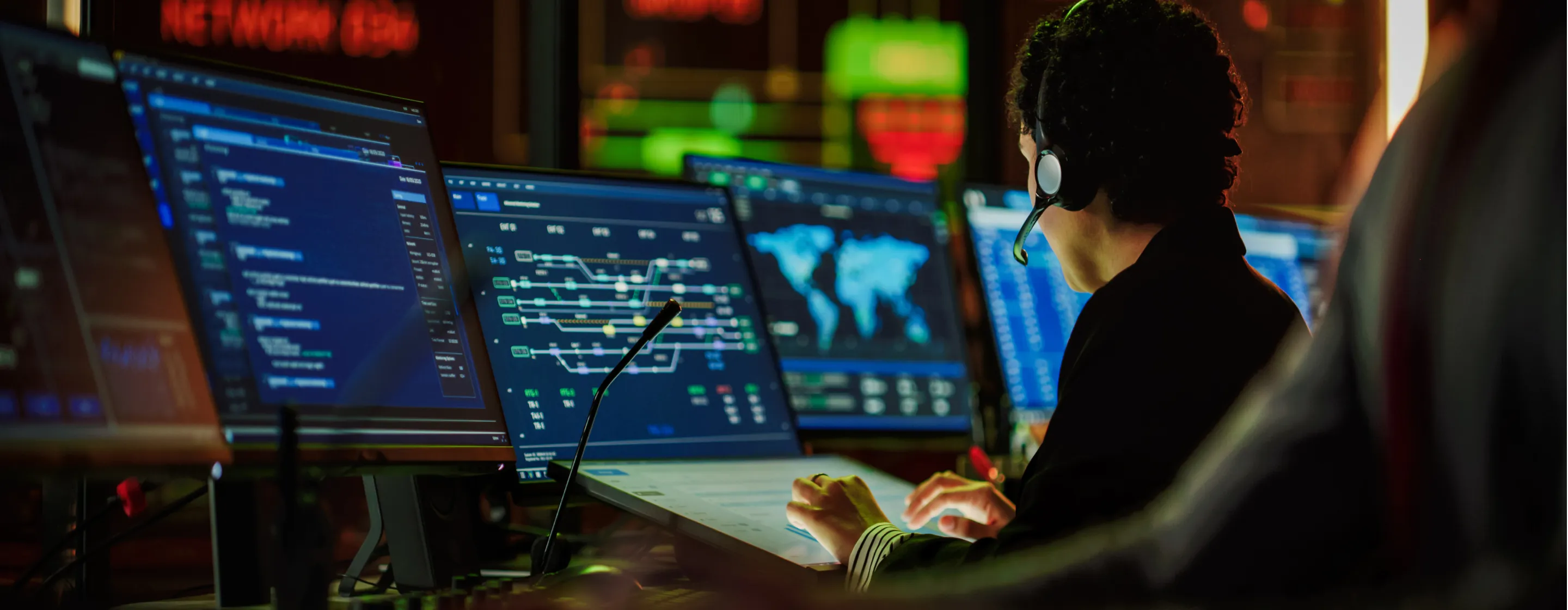 A professional wearing a headset and typing on a computer in a monitoring control room.