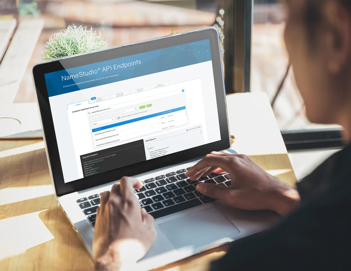A man sitting at a desk in a sunny room and typing on his laptop.