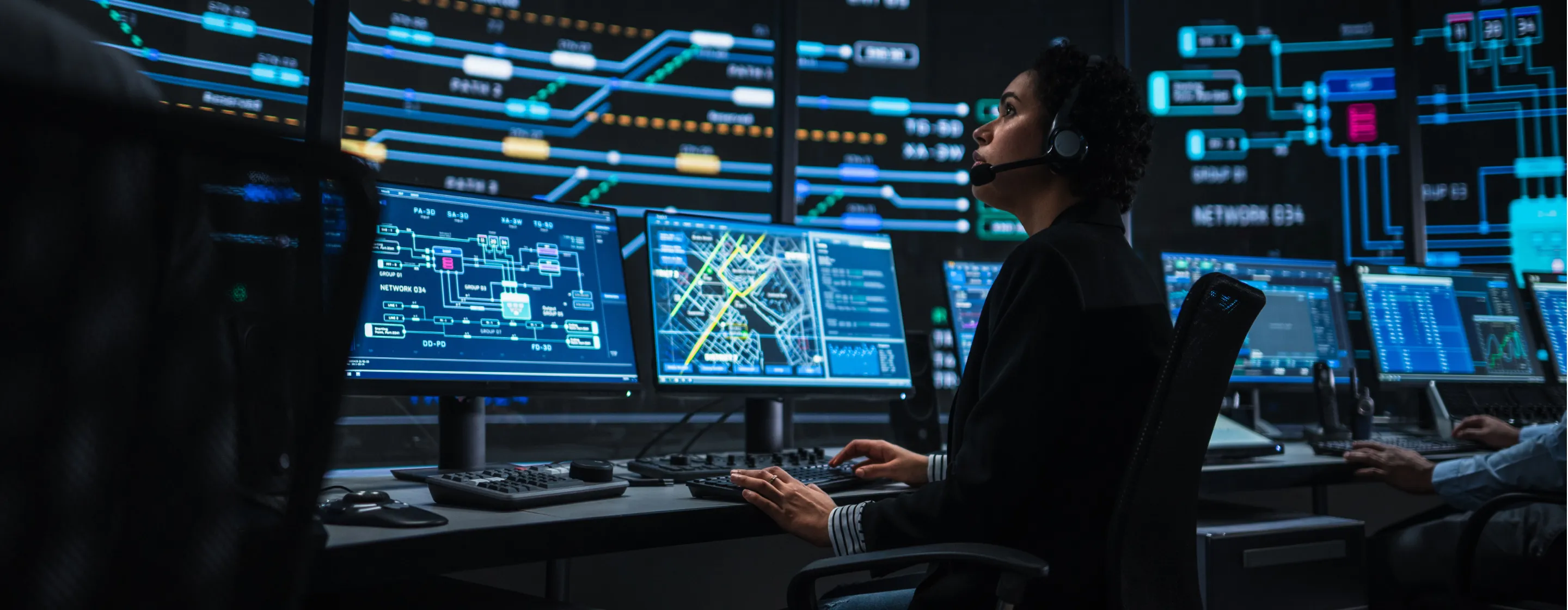 IT technical support specialist working on multiple digital screens with bright network maps in a monitoring control room.
