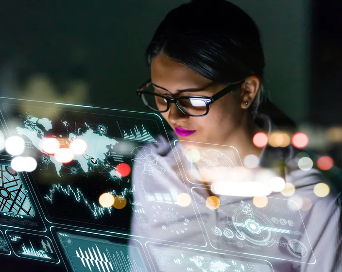 A woman examining a futuristic interface screen with multiple dashboards of maps covered with an overlay of city lights.