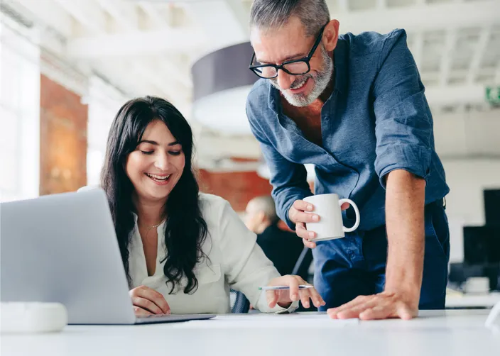 Two colleagues in front of a laptop who are smiling and collaborating on a project together in an open office setting.