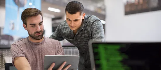 Two colleagues working on a project on both a tablet and computer in an open-concept office.