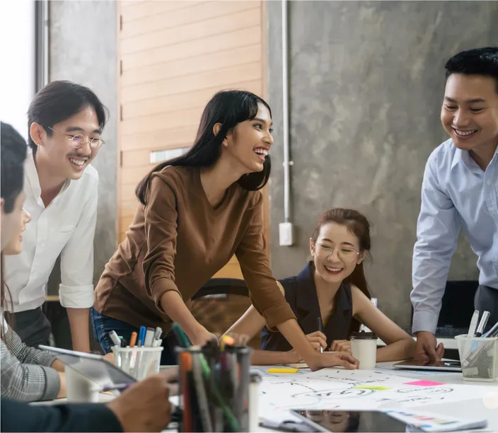 Business colleagues who are standing and sitting in an office while they smile and happily work together on a project.