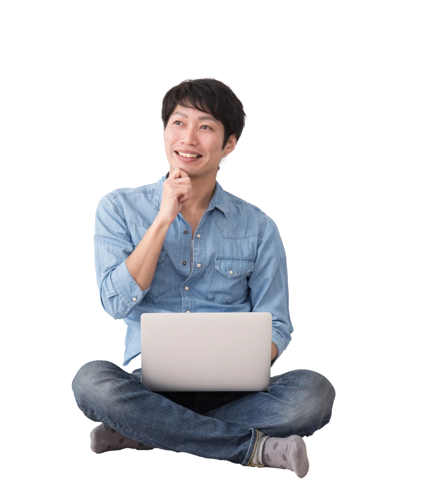 A smiling man sitting cross-legged on the floor while contemplating an idea on his laptop and looking off into the distance.